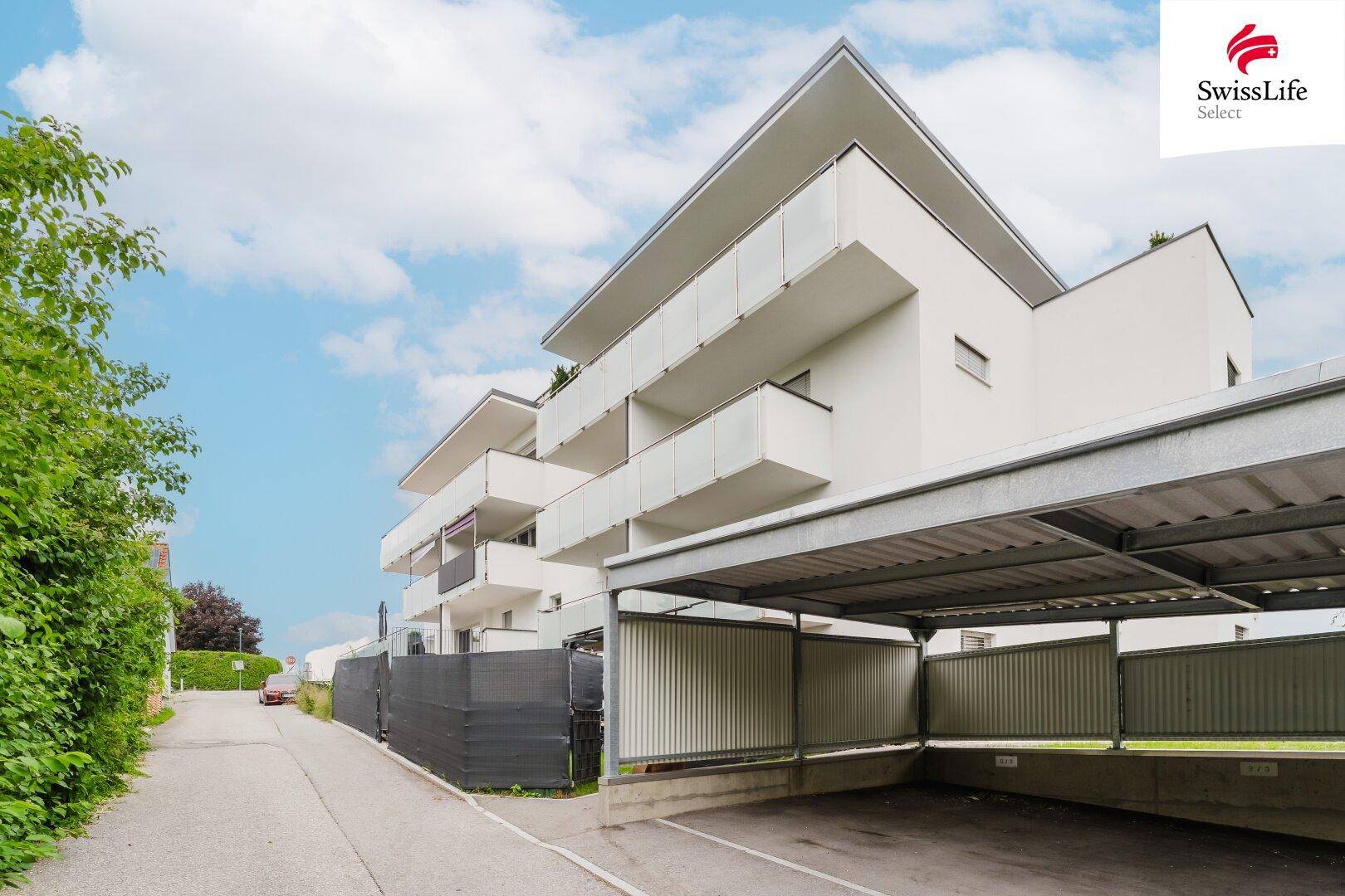 Modernes Mehrfamilienhaus mit Balkonen und überdachten Stellplätzen.