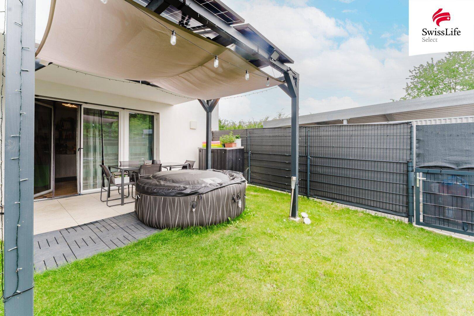 Gepflegter Gartenbereich mit Rasenfläche, überdachter Terrasse und Whirlpool.