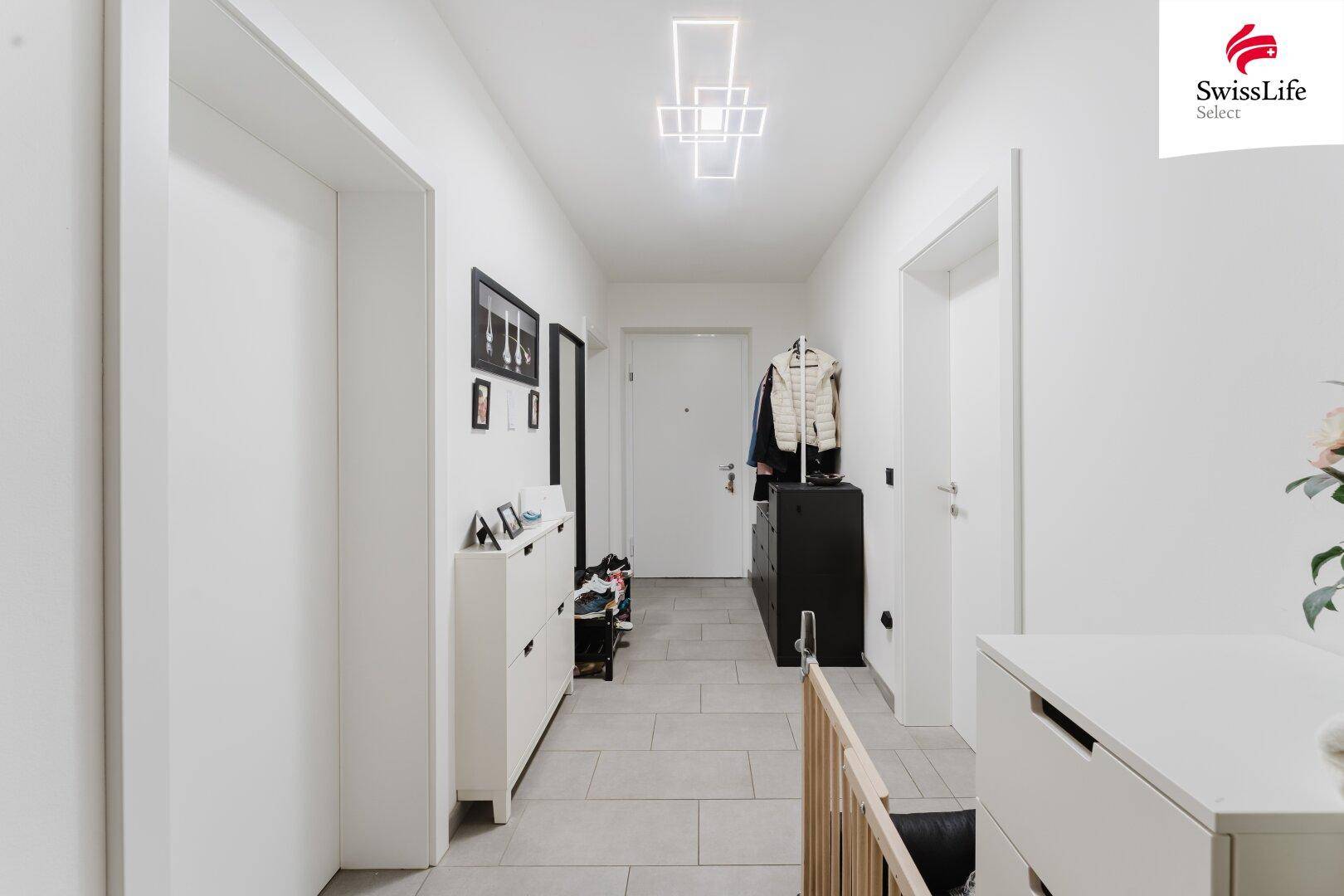 Heller Flur mit modernen Fliesen, Garderobe und schlichten weißen Türen.