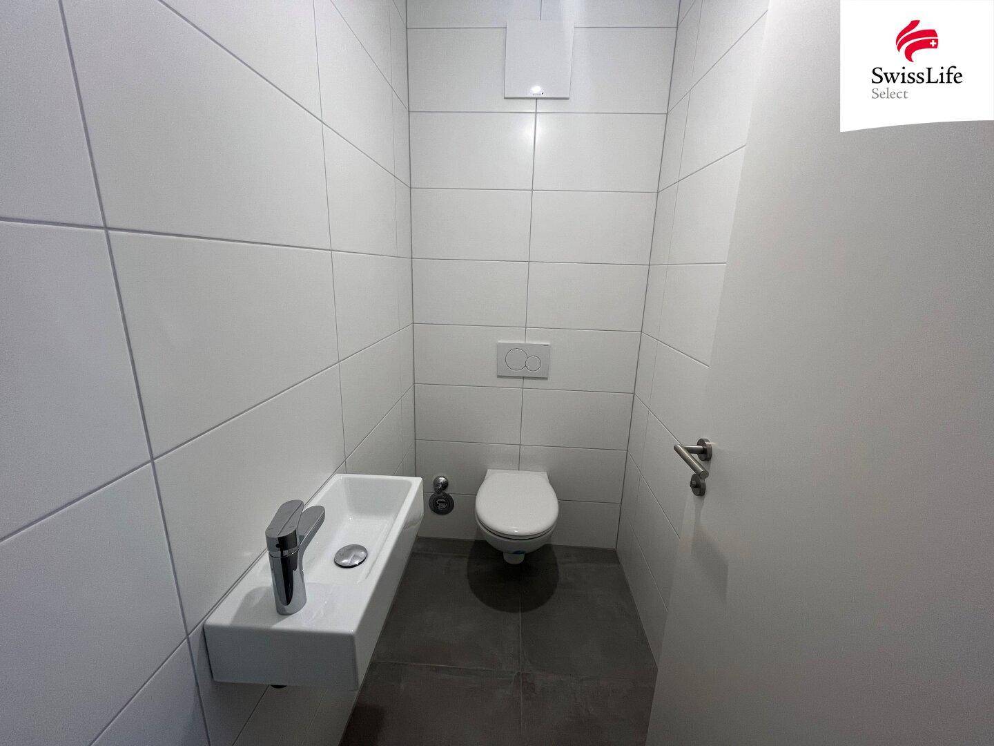Modernes Gäste-WC mit Wand-WC und kleinem Handwaschbecken, komplett gefliest.