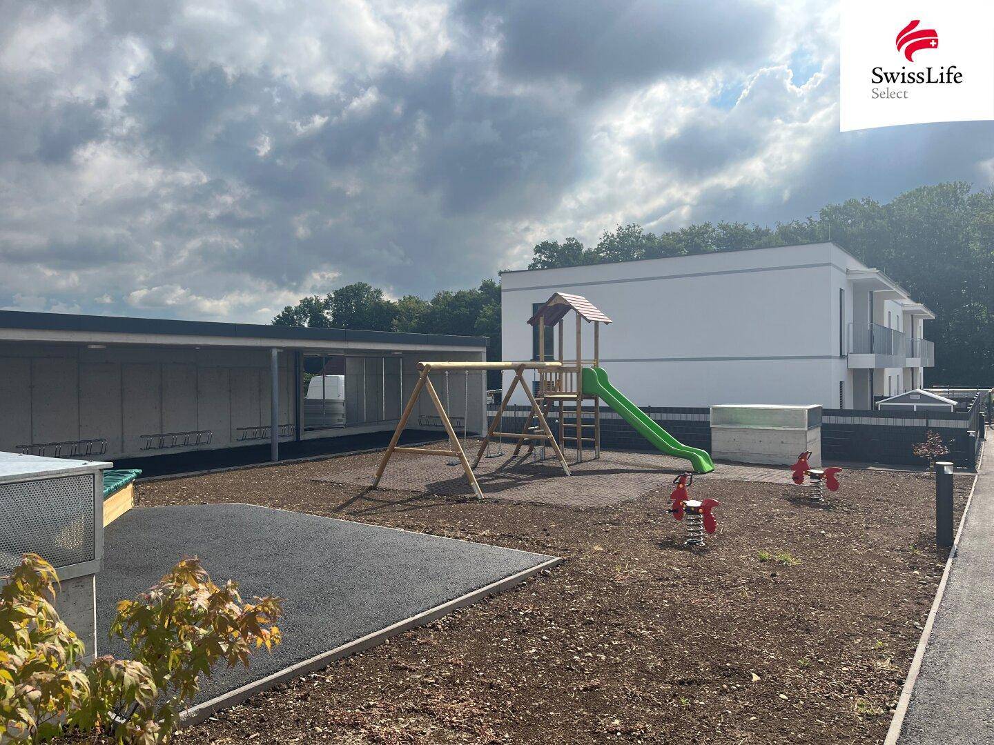 Kinderspielplatz mit Rutsche und Schaukeln, umgeben von einem Neubaugebiet.