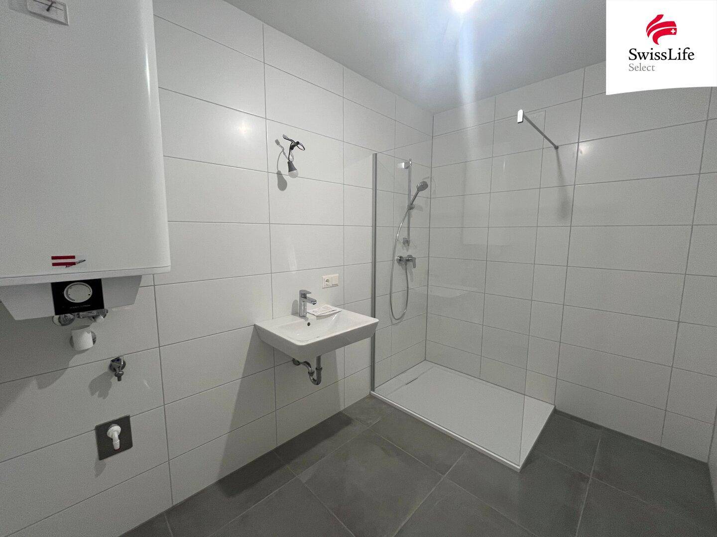 Modernes Badezimmer mit Fliesen, Dusche und Waschbecken, ausgestattet mit einem Warmwasserboiler.