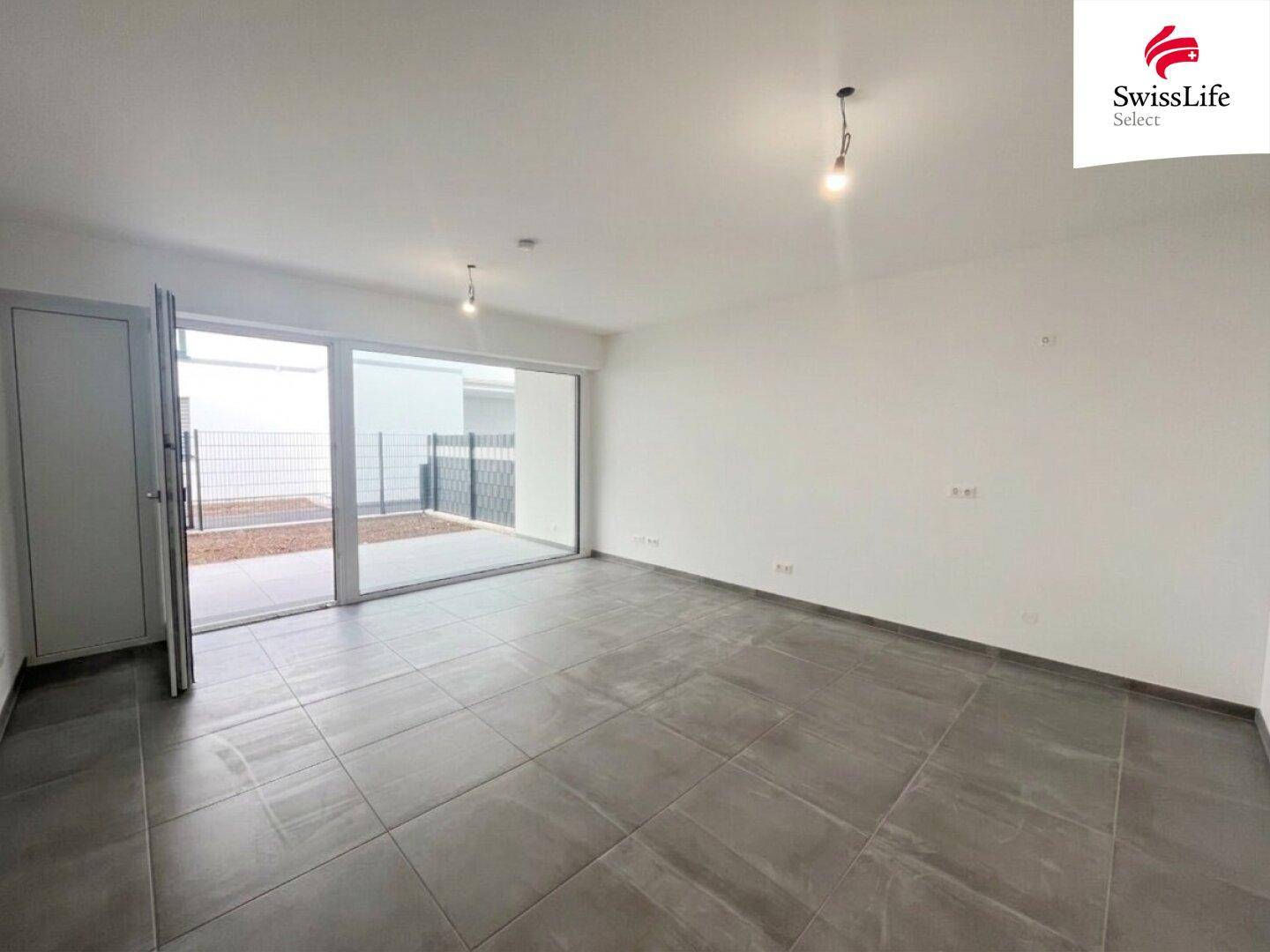 Helles, leeres Wohnzimmer mit großen Schiebetüren und Zugang zu einer Terrasse.