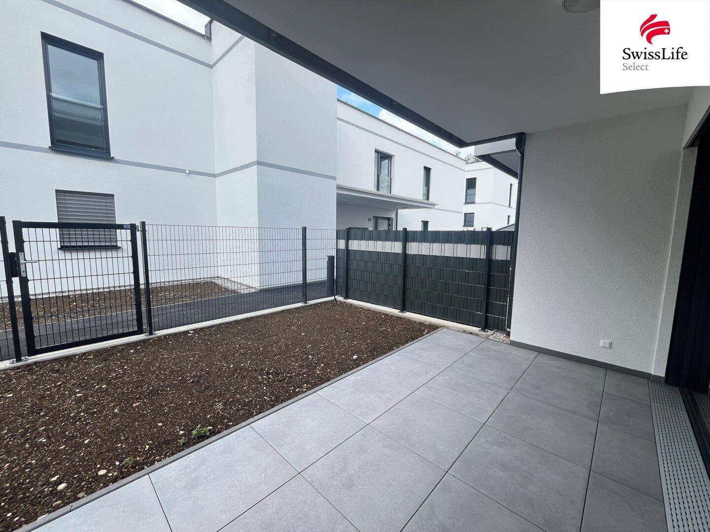 Neu angelegte Terrasse mit Fliesen und vorbereitetem Gartenbereich, umgeben von einem Zaun.