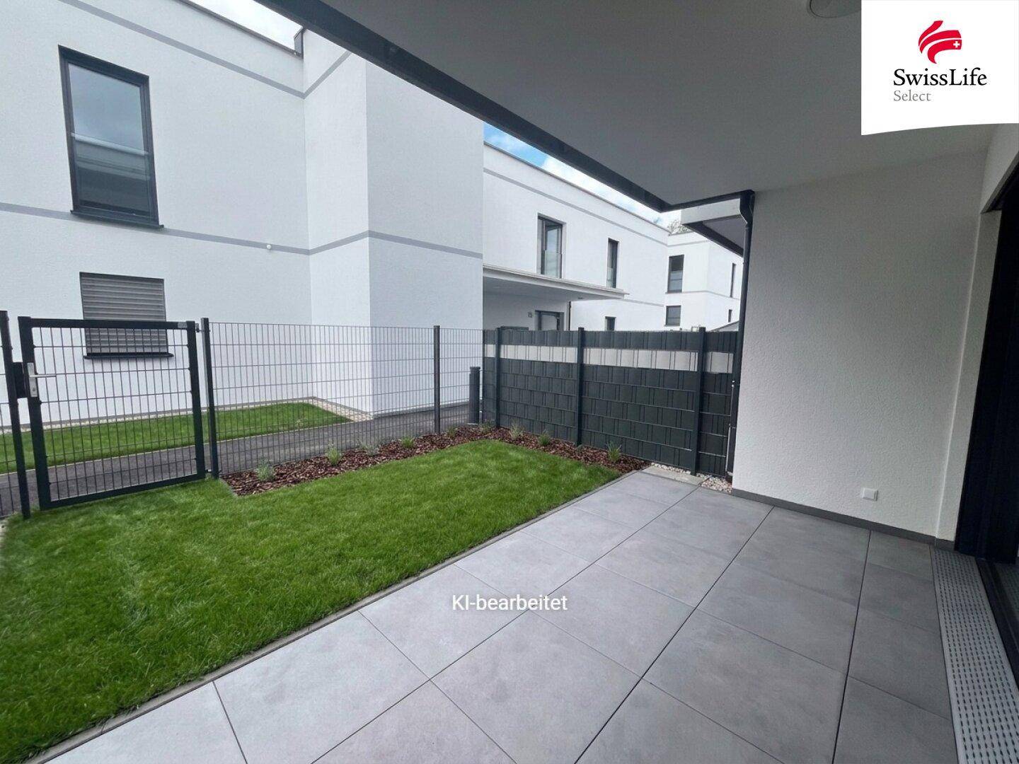 Moderne Terrasse mit Fliesenboden und kleinem Rasenbereich, umgeben von einem Zaun.