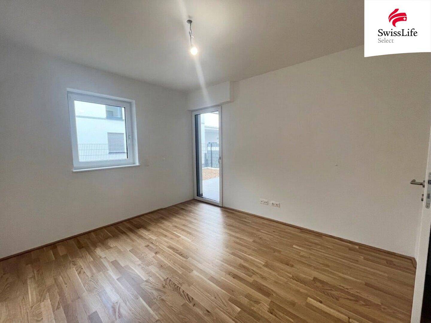 Helles Schlafzimmer mit Holzboden und Zugang zu einem kleinen Außenbereich.