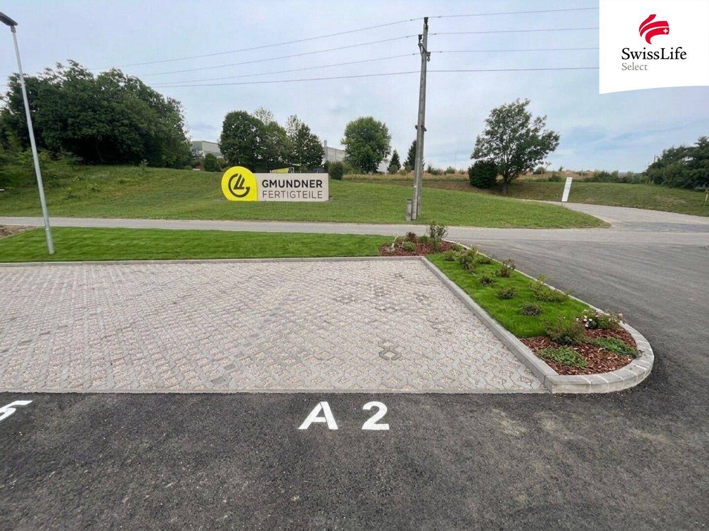 Außenparkplatz mit gepflasterten Flächen und Grünstreifen, umgeben von Natur.