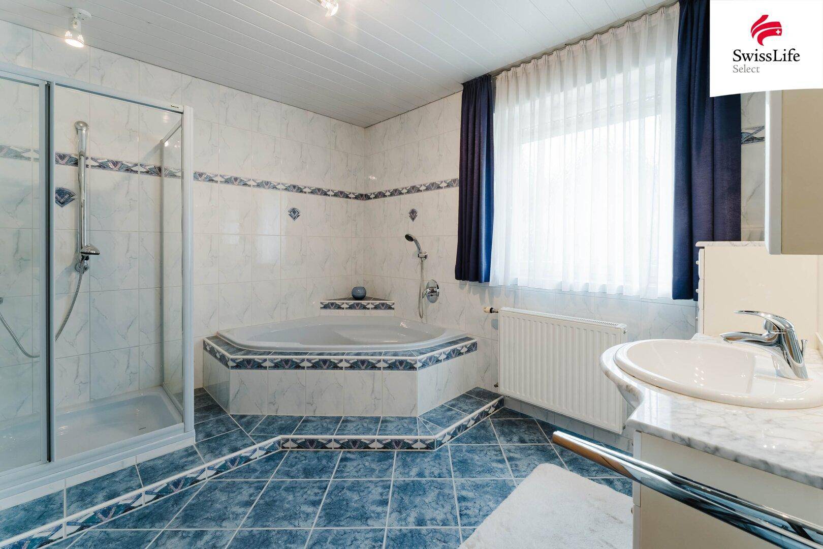 Badezimmer mit Eckbadewanne, separater Dusche und blauen Fliesen im 80er-Jahre-Stil.