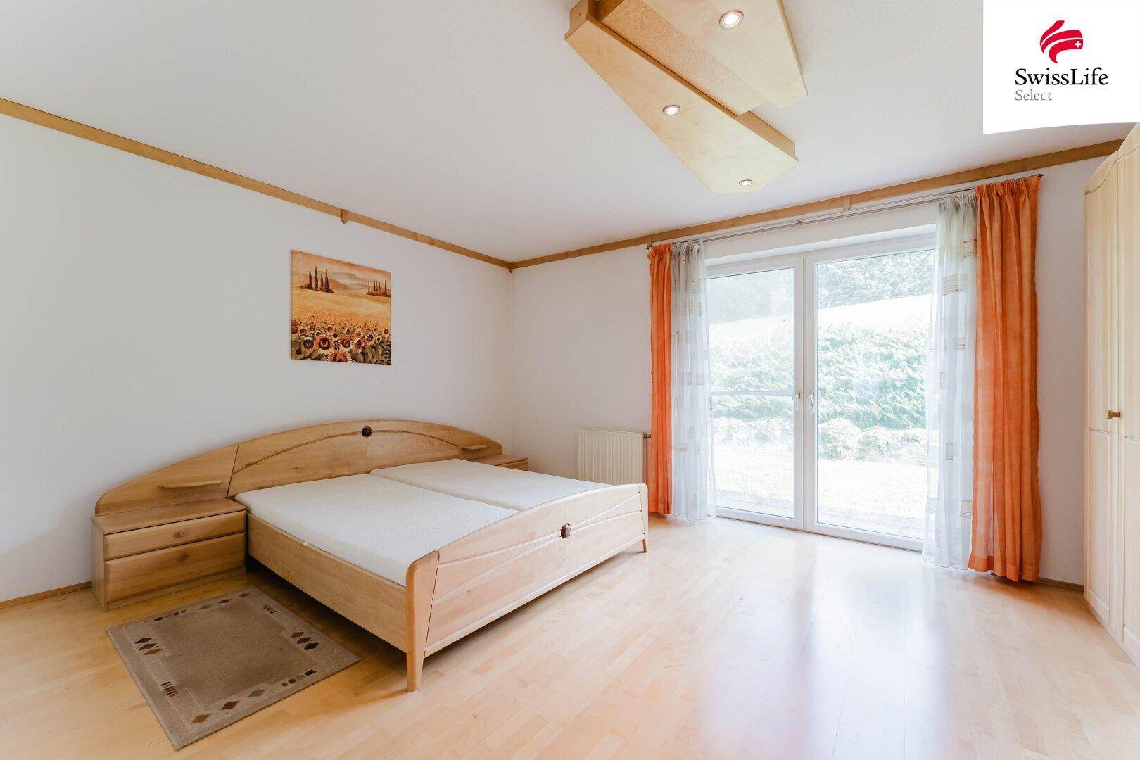 Helles Schlafzimmer mit Doppelbett aus Holz, Parkettboden und Zugang zum Garten.