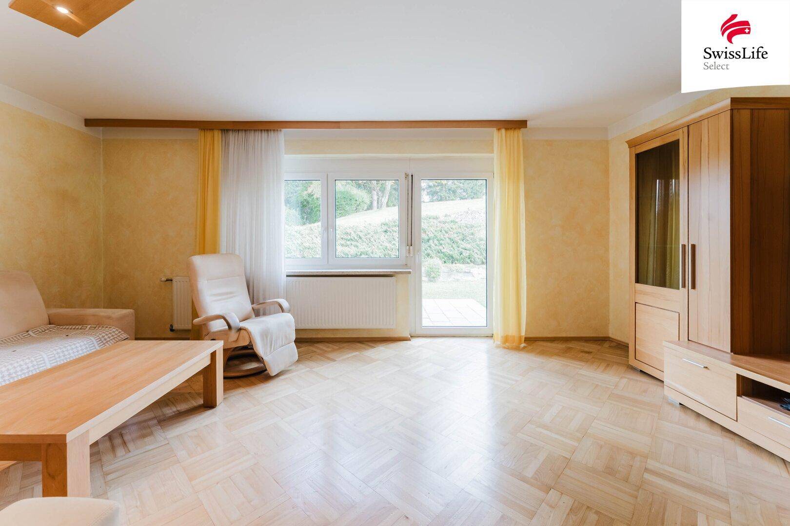 Gemütliches Wohnzimmer mit Parkettboden, hellem Sofa und großem Fenster zum Garten.