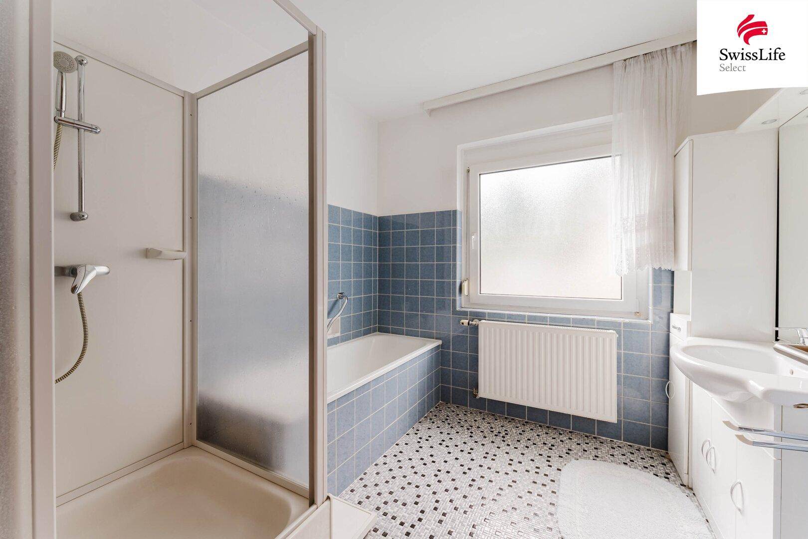 Badezimmer mit Badewanne, separater Dusche und blauen Fliesen im 80er-Jahre-Stil.