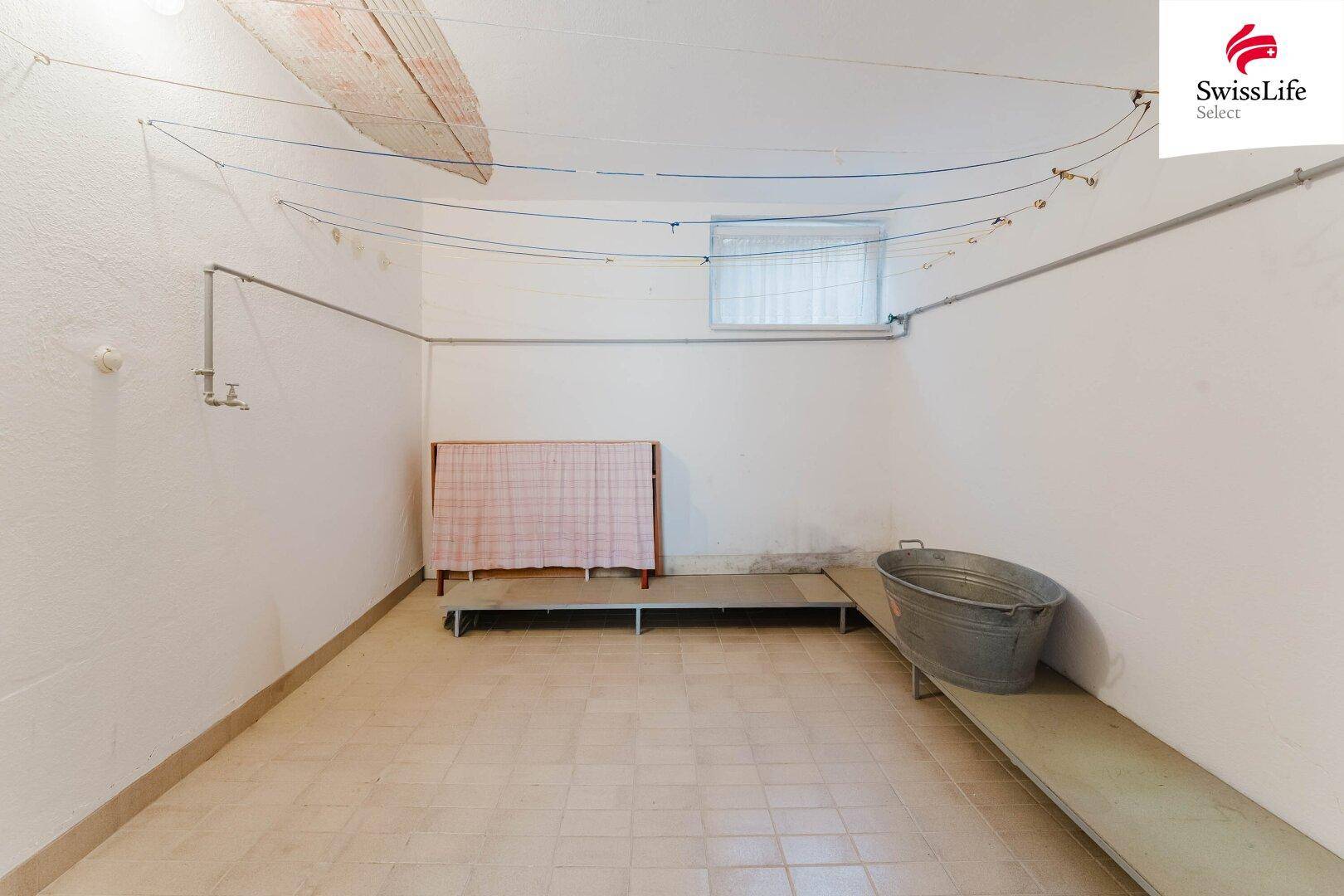 Einfacher Waschraum im Keller mit Wäscheleinen und Fliesenboden.