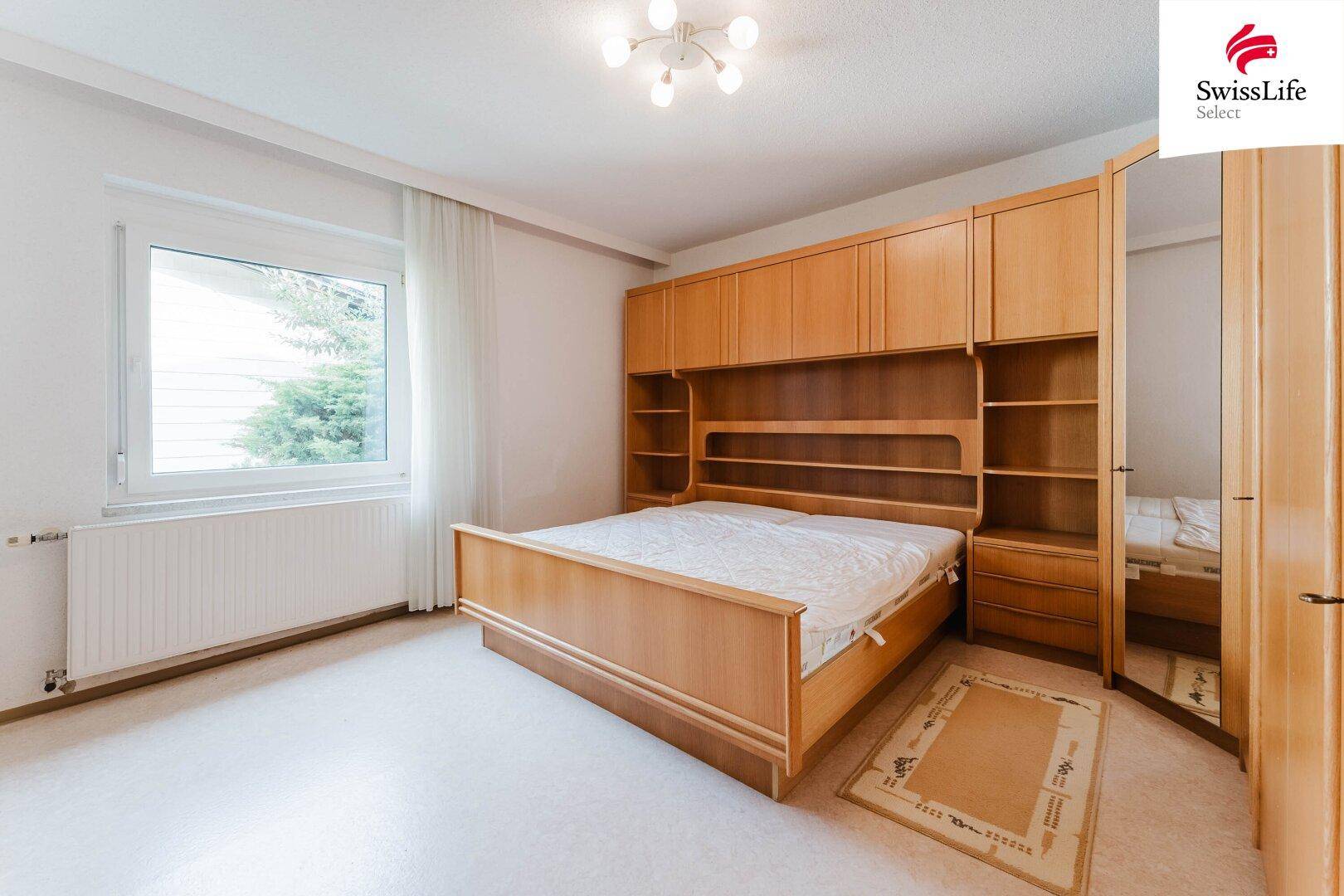 Schlafzimmer mit großem Holzbett, Einbauschränken und Teppichboden.
