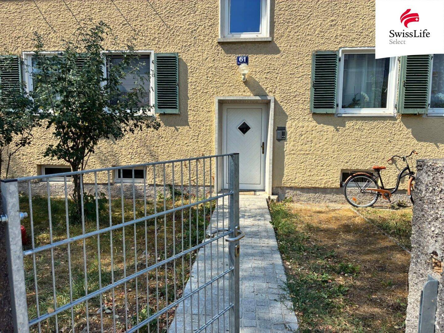 Eingangsbereich des Hauses mit weißer Tür, Hausnummer 61 und einem kleinen Vorgarten.