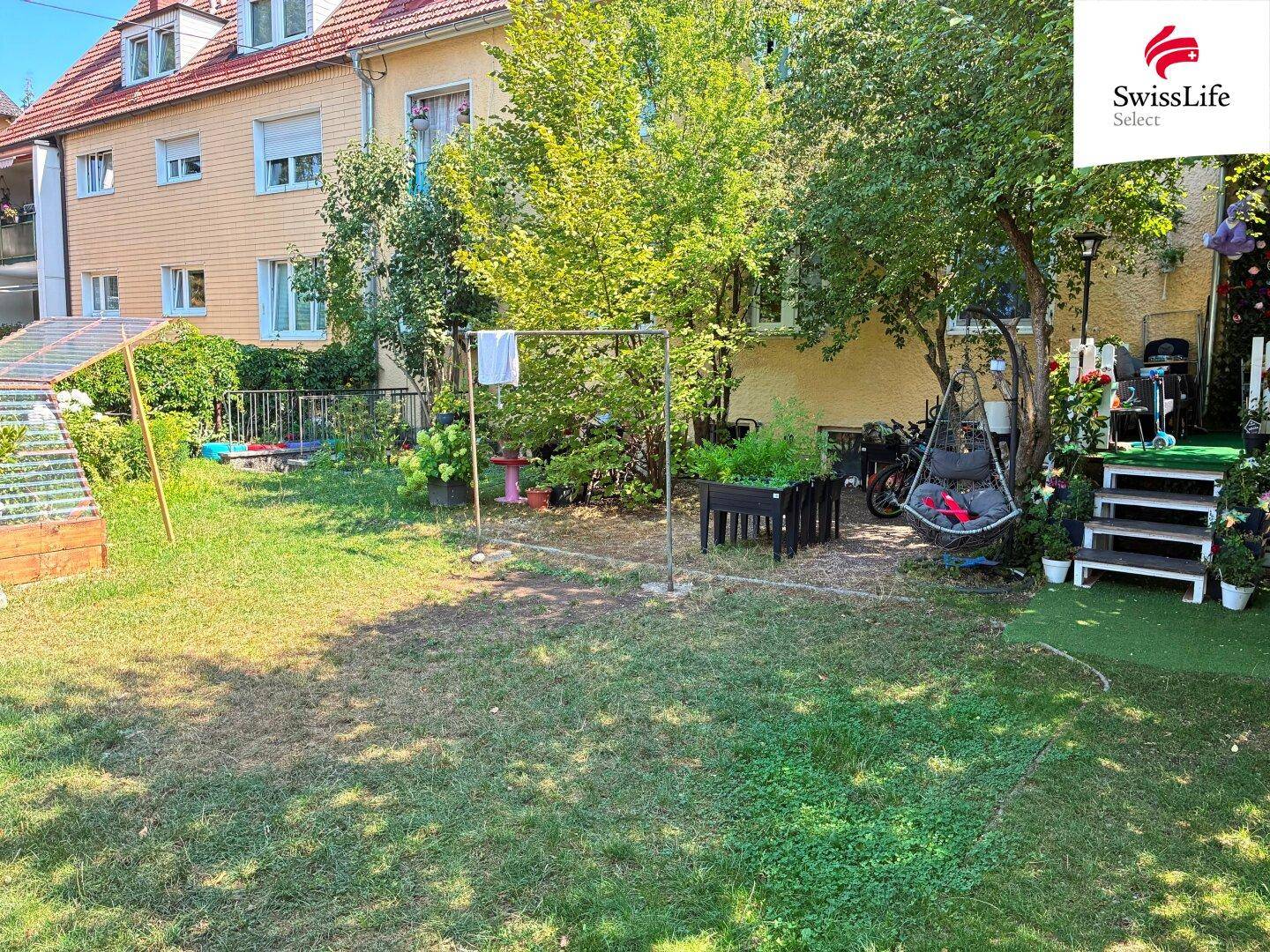 Gepflegter Hinterhofgarten mit Rasenfläche, Schaukelstuhl, Grillbereich und verschiedenen Pflanzen.