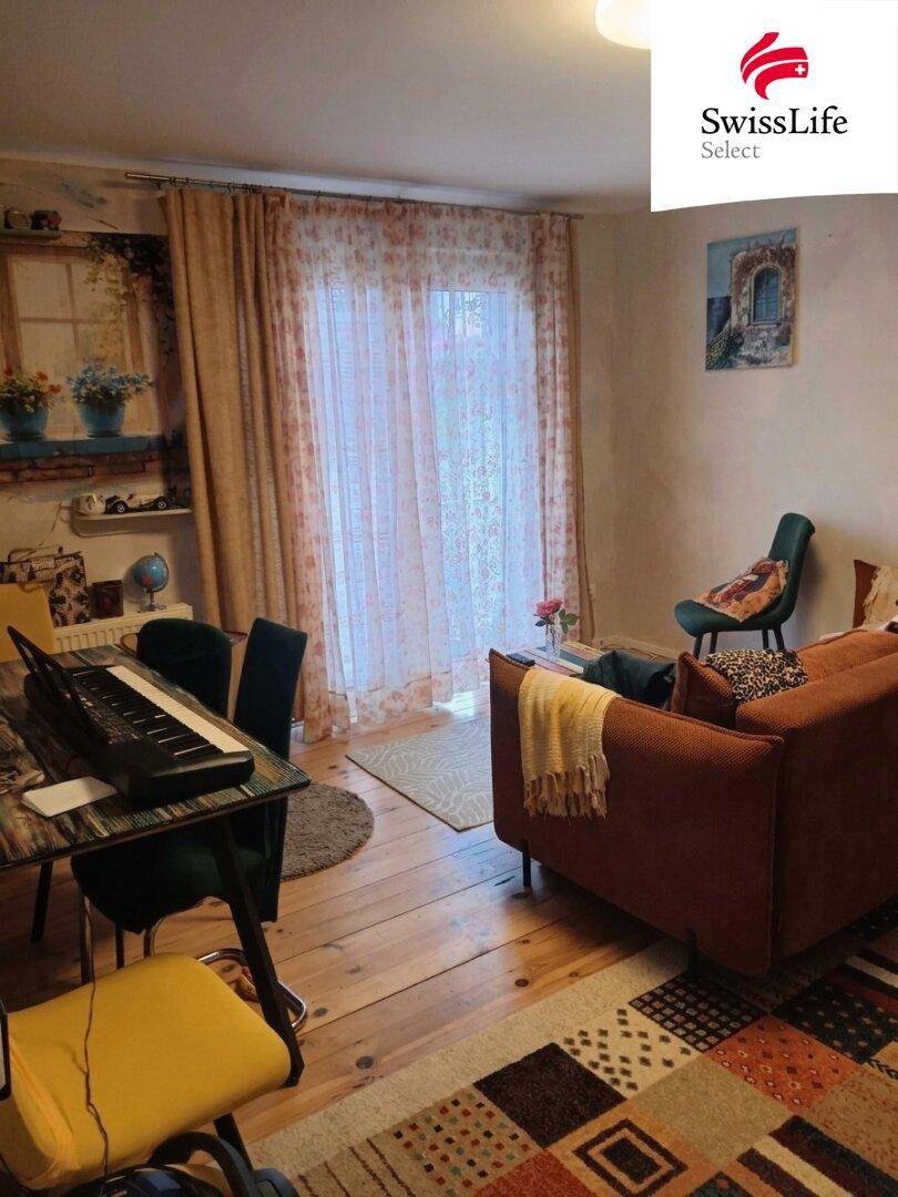 Gemütlicher Wohn- und Essbereich mit Holzboden, Teppich und Zugang zu einem Balkon oder einer Terrasse.