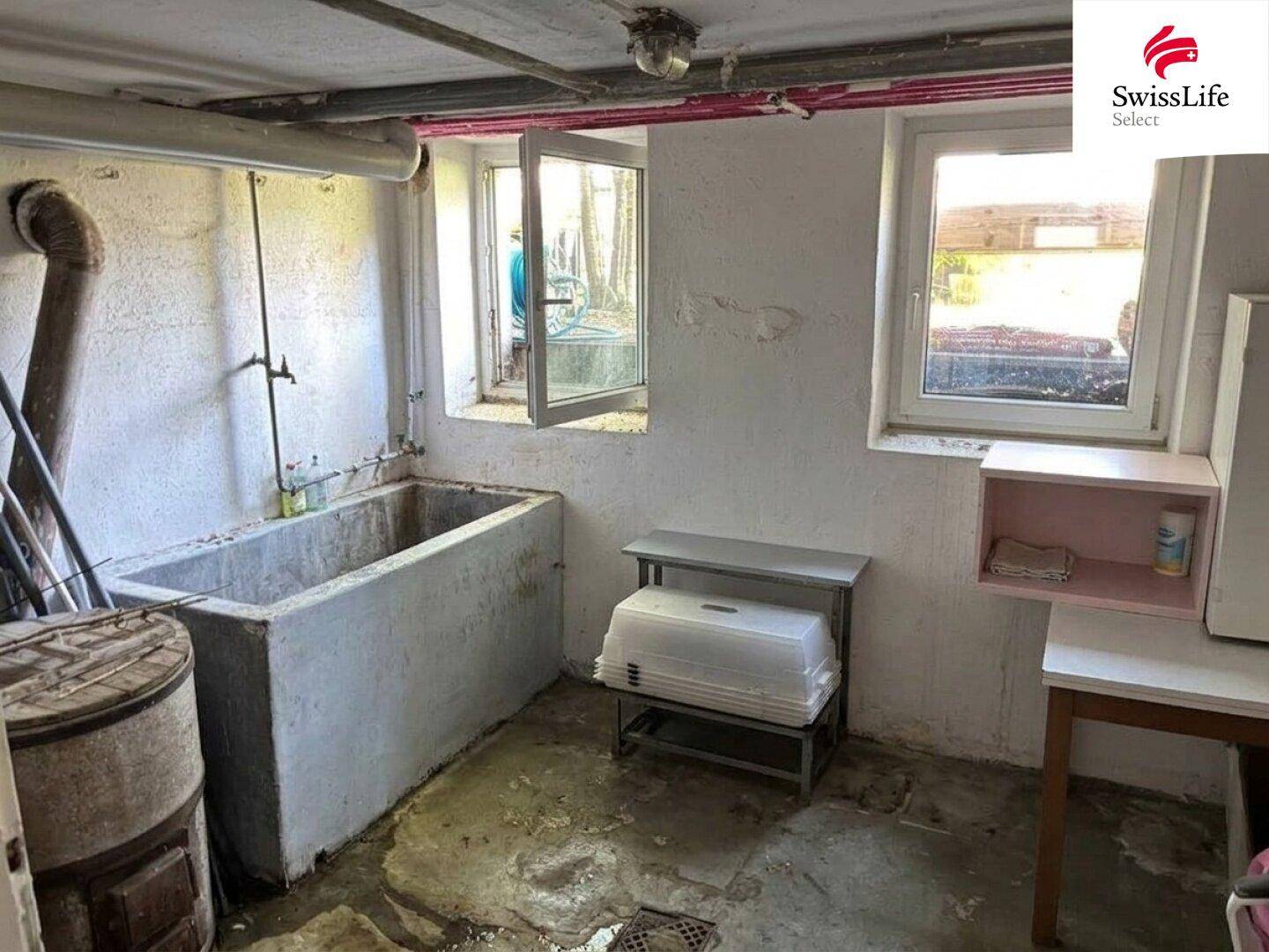 Waschküche im Keller mit großem Waschbecken, Fenstern und einfacher Ausstattung für den Hausgebrauch.