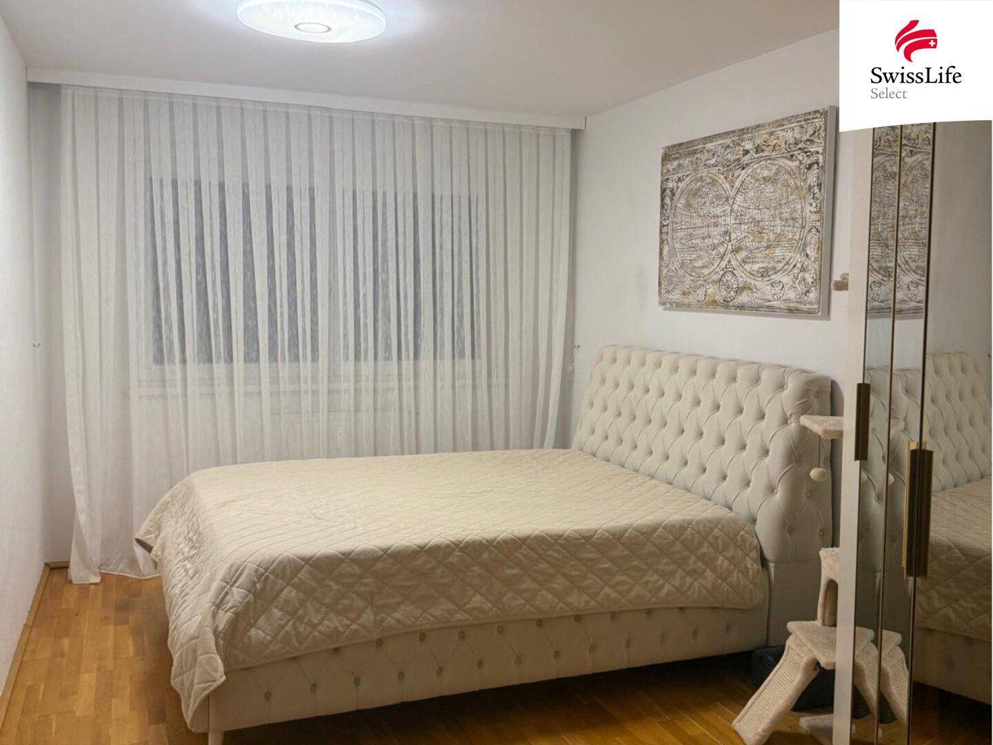 Helles Schlafzimmer mit großem Doppelbett und elegantem Kopfteil, ausgestattet mit einem Spiegelschrank.