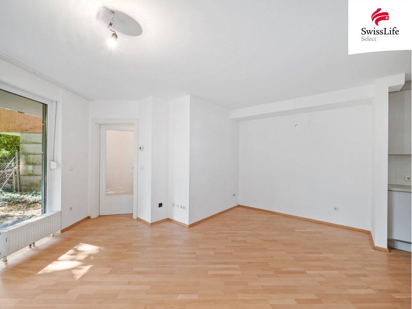 Leerer Wohnbereich mit Holzfußboden und einem angrenzenden, offenen Küchenbereich.