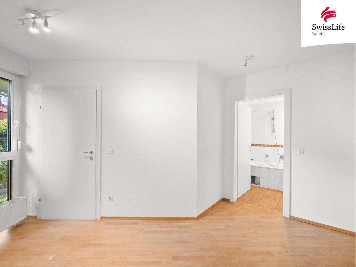 Heller Raum mit Holzfußboden und einem offenen Durchgang zu einem Badezimmer.