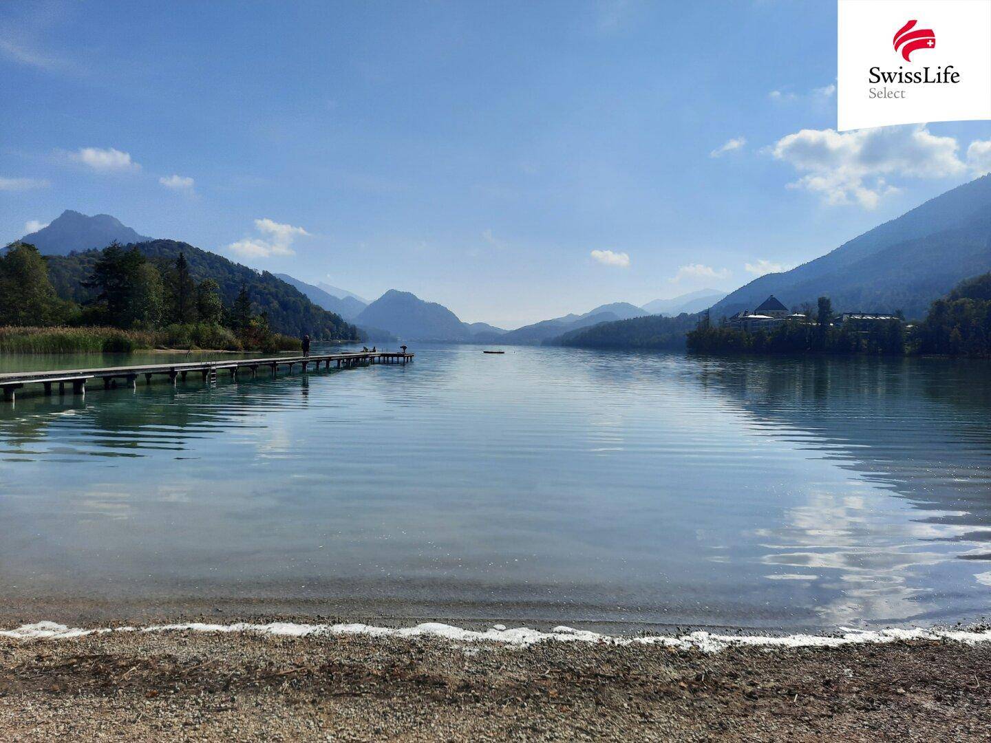 Malerischer See mit Holzsteg und beeindruckender Bergkulisse unter klarem Himmel.