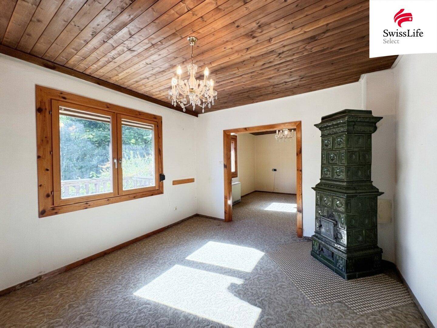Gemütliches Wohnzimmer mit traditionellem Kachelofen, Holzbalkendecke und Teppichboden.