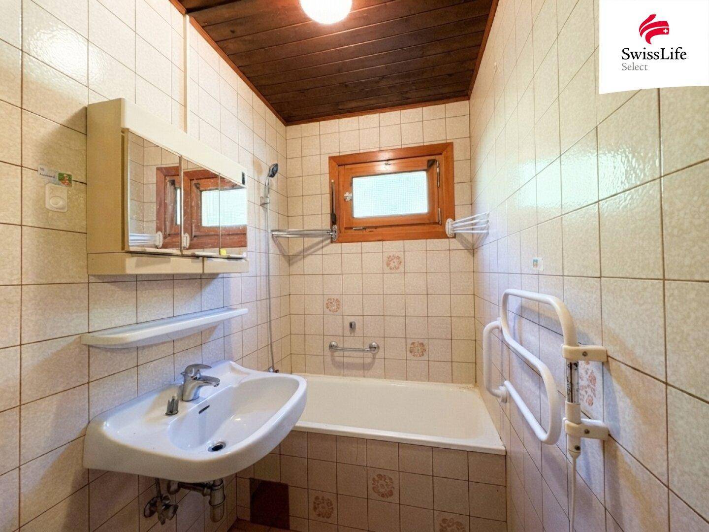 Badezimmer mit Badewanne, Waschbecken, Spiegelschrank und hellen Fliesen an Wänden und Boden.