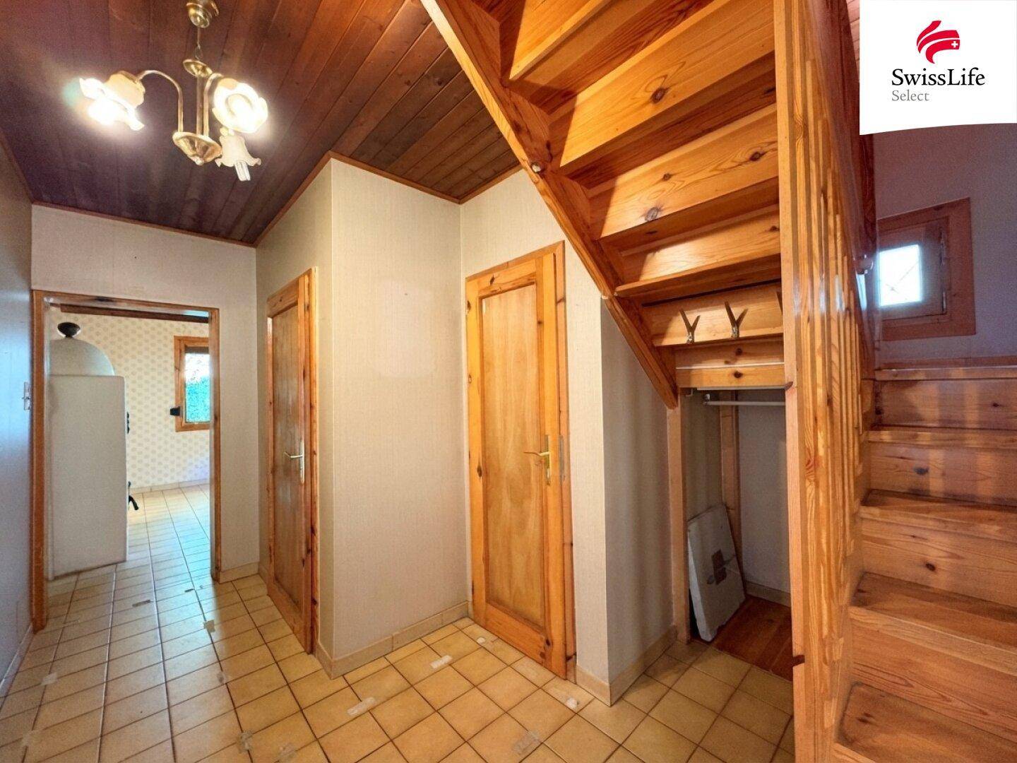 Flur mit Holztreppe, Fliesenboden und Holztüren, der zu den oberen Etagen führt.