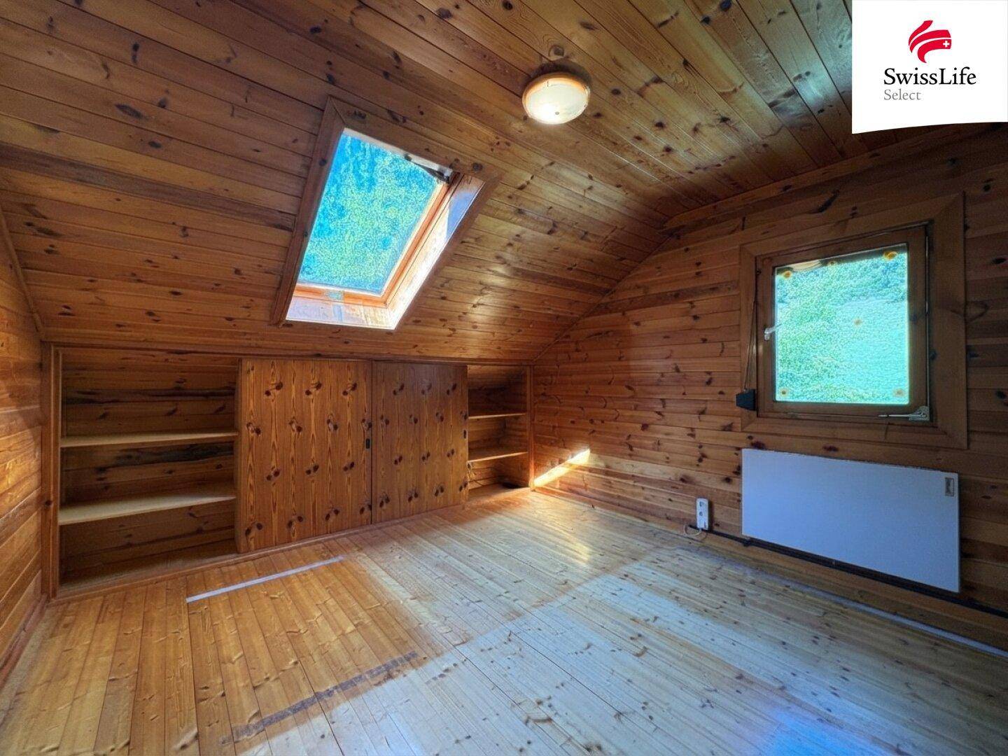 Dachzimmer mit Holzverkleidung, Holzboden, Dachfenster und integrierten Schränken.
