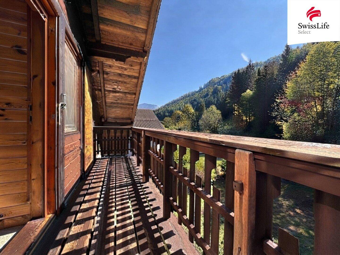 Holzbalkon mit malerischem Blick auf die umliegende Berglandschaft und viel Grün.