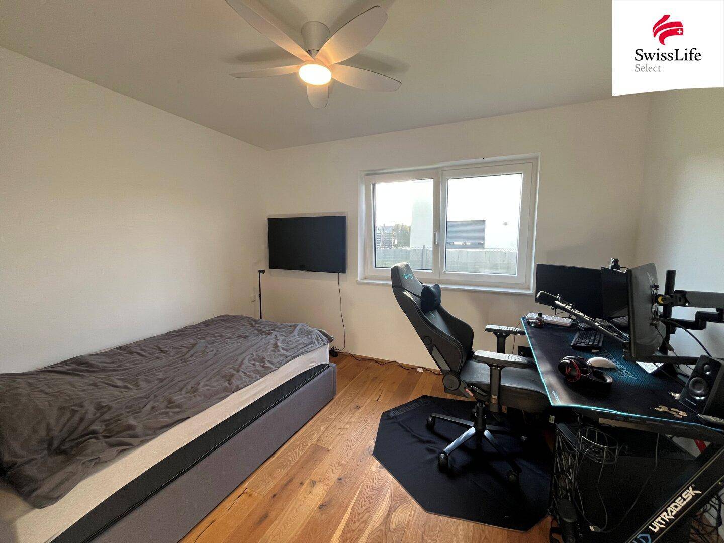 Modern eingerichtetes Schlafzimmer mit Einzelbett, Gaming-Setup und Deckenventilator.