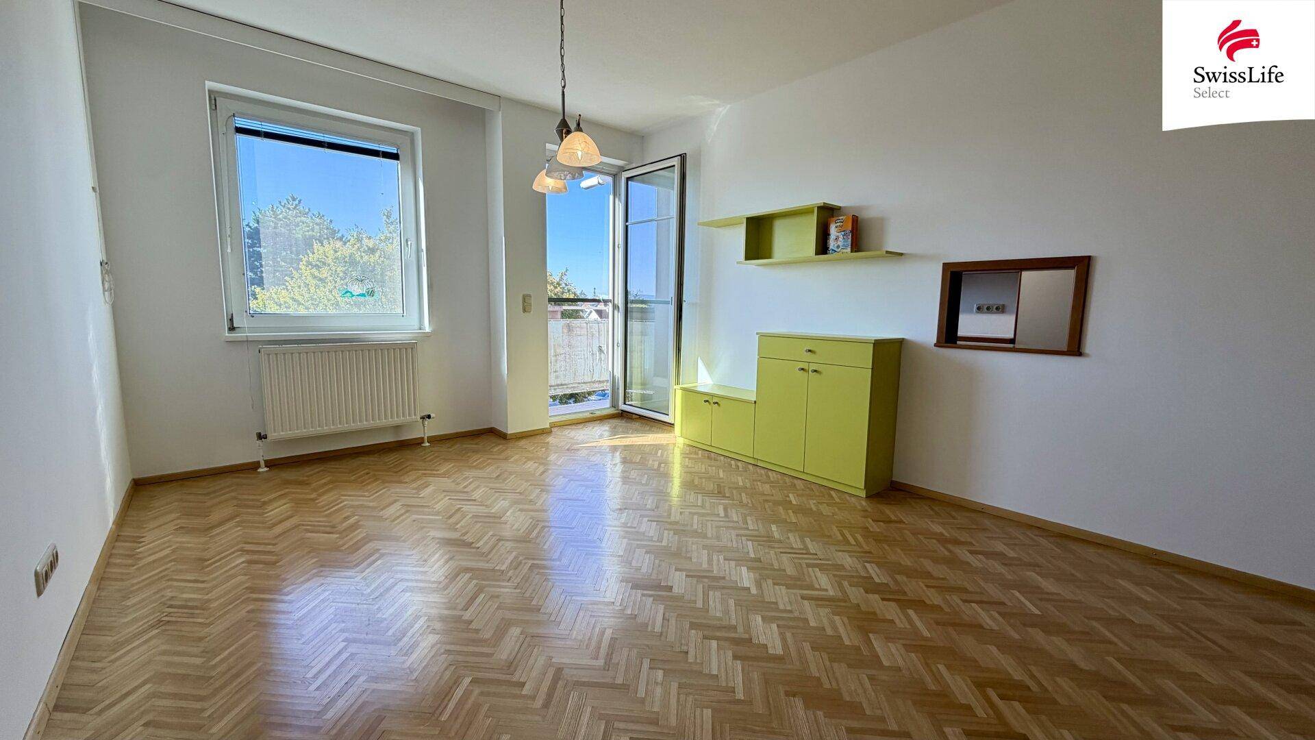 Geräumiges Wohnzimmer mit Fischgrätparkett, Balkonzugang und hellen Wänden.