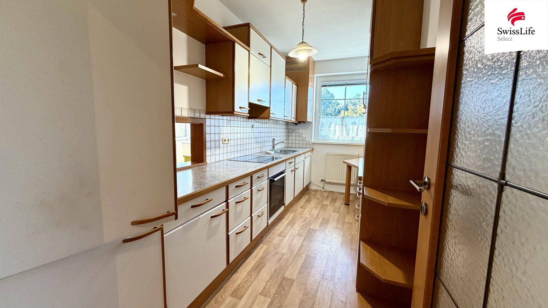 Funktionale Küche mit Holzschränken, weißen Fronten, Fliesenrückwand und Fenster.