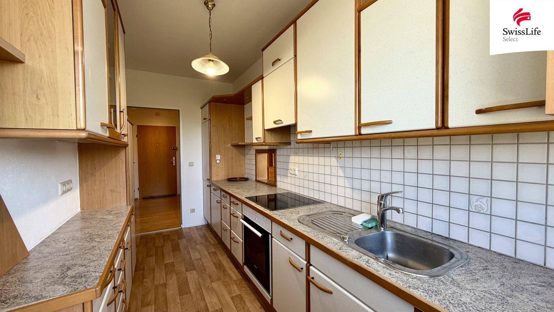 Funktionale Küche mit Holzschränken, weißen Fronten, Fliesenrückwand und Spüle.