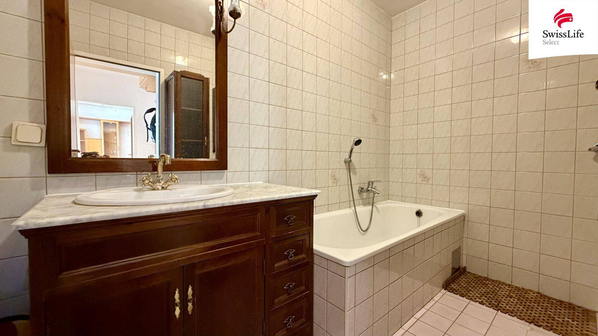 Badezimmer mit Badewanne, Waschtisch mit Marmorplatte und Fliesen an den Wänden.