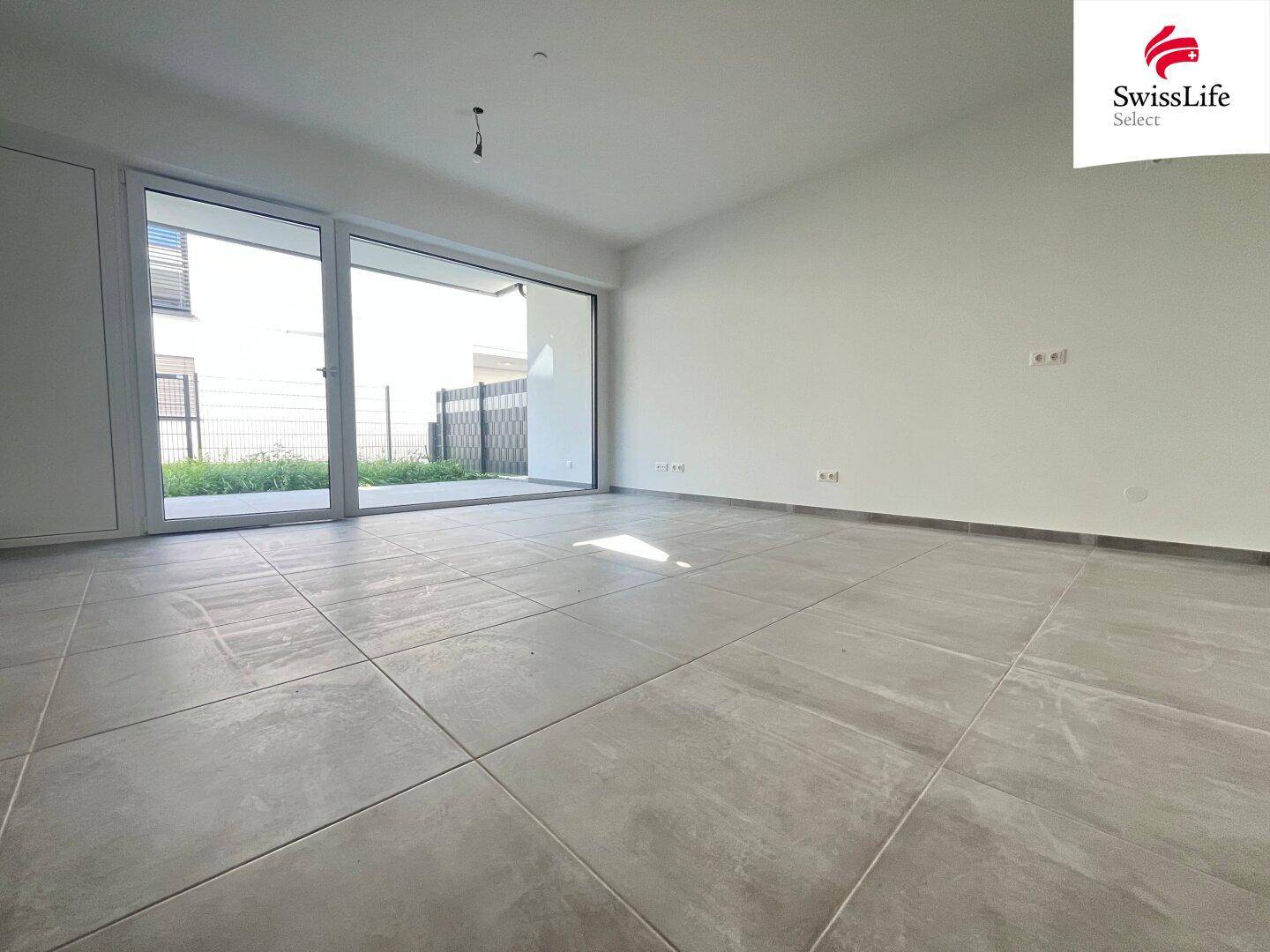 Heller, leerer Wohnraum mit großen Fliesen und Zugang zur Terrasse im Erdgeschoss.