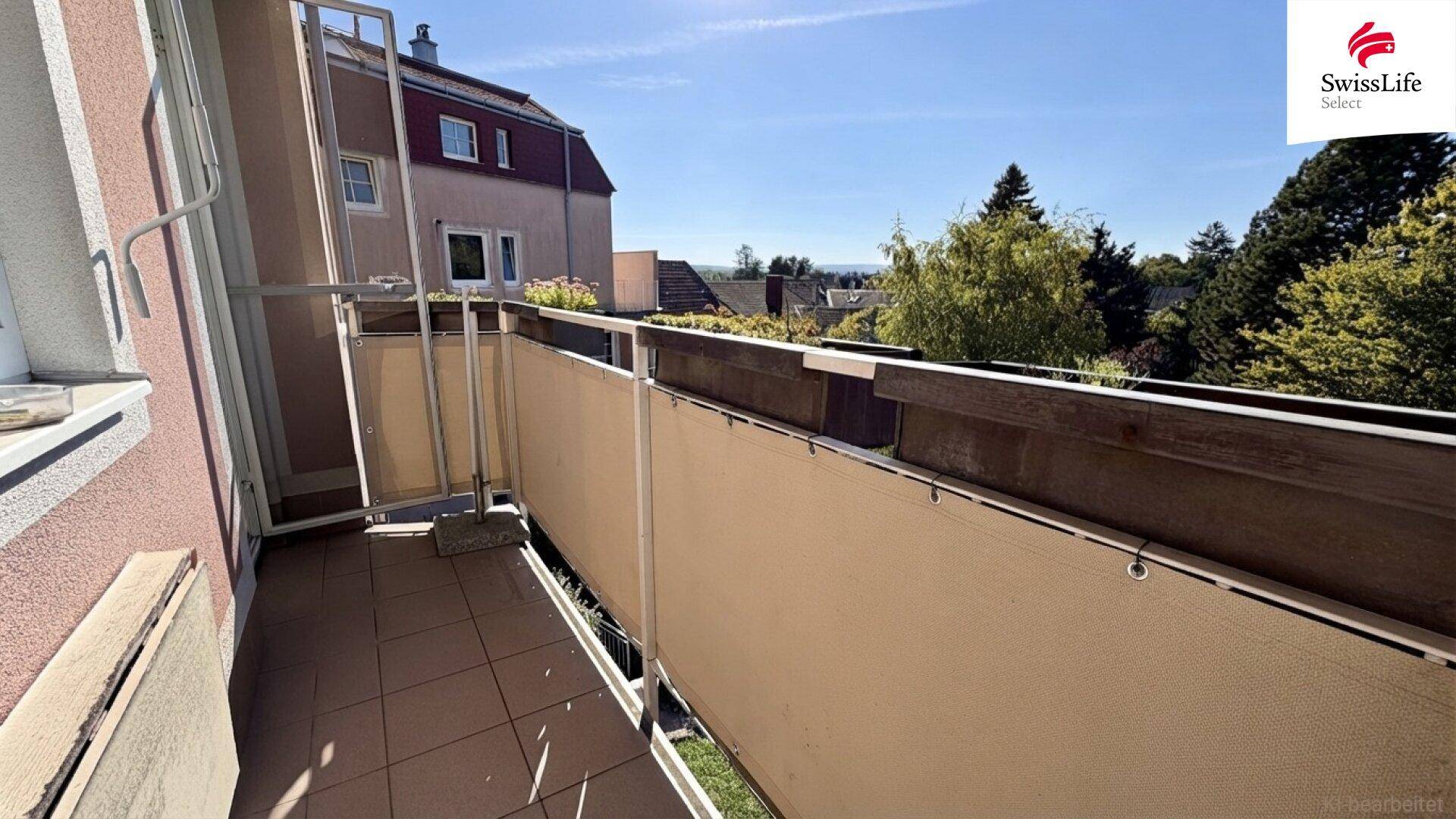 Balkon mit Fliesenboden, Sichtschutz und Blick auf die umliegenden Gebäude und Bäume.
