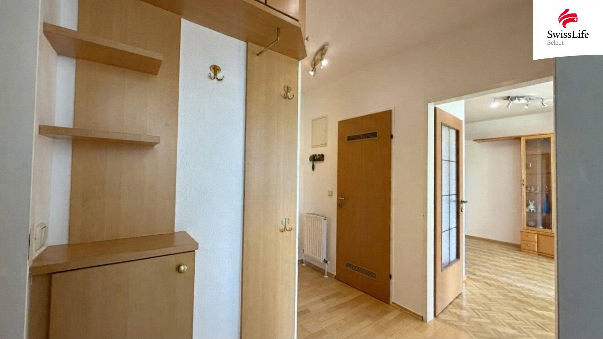Eingangsbereich mit Holzmöbeln, Garderobe und Parkettboden, der zu weiteren Räumen führt.