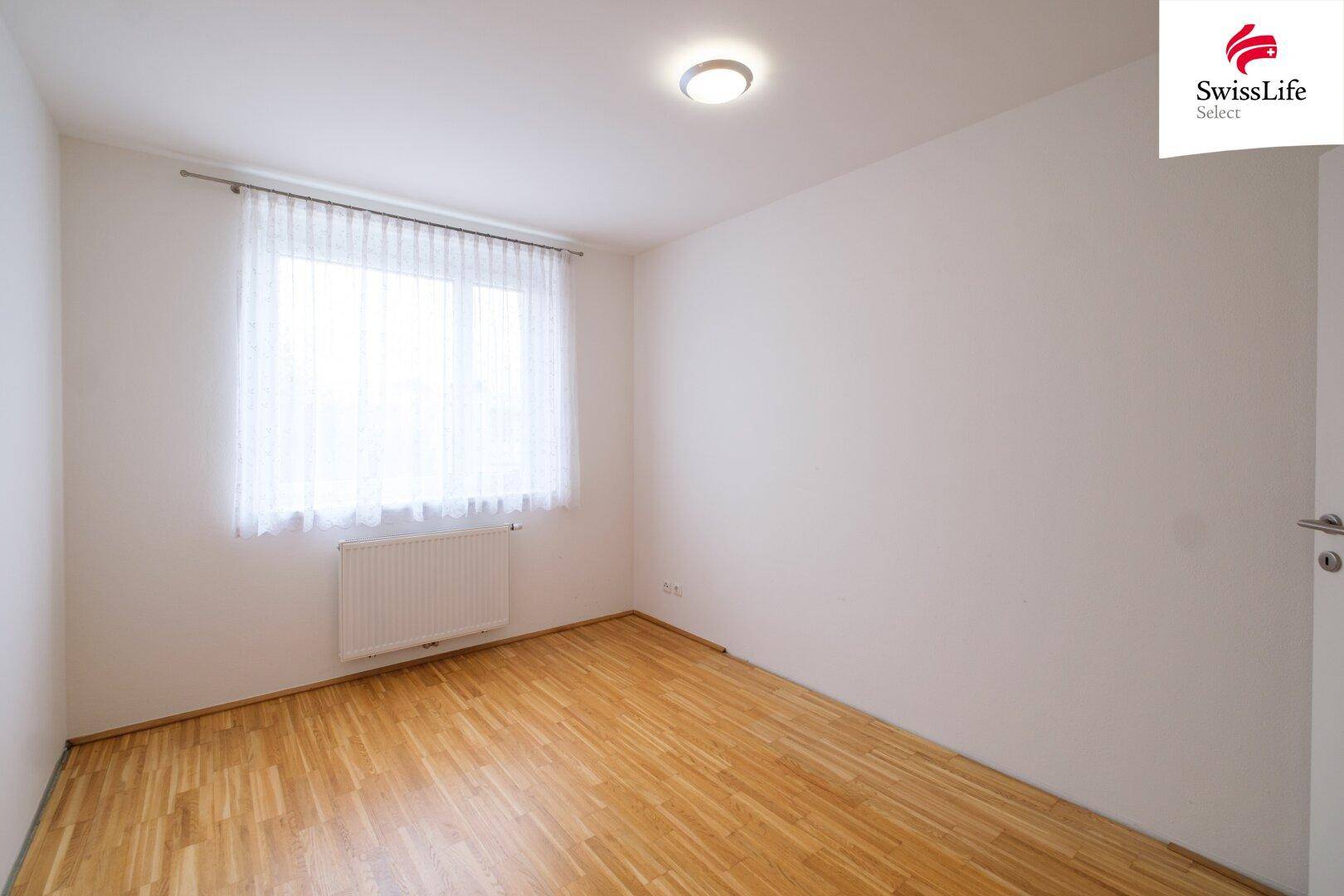 Leeres Zimmer mit Parkettboden, weißen Wänden und einem Fenster, ideal als Schlafzimmer.