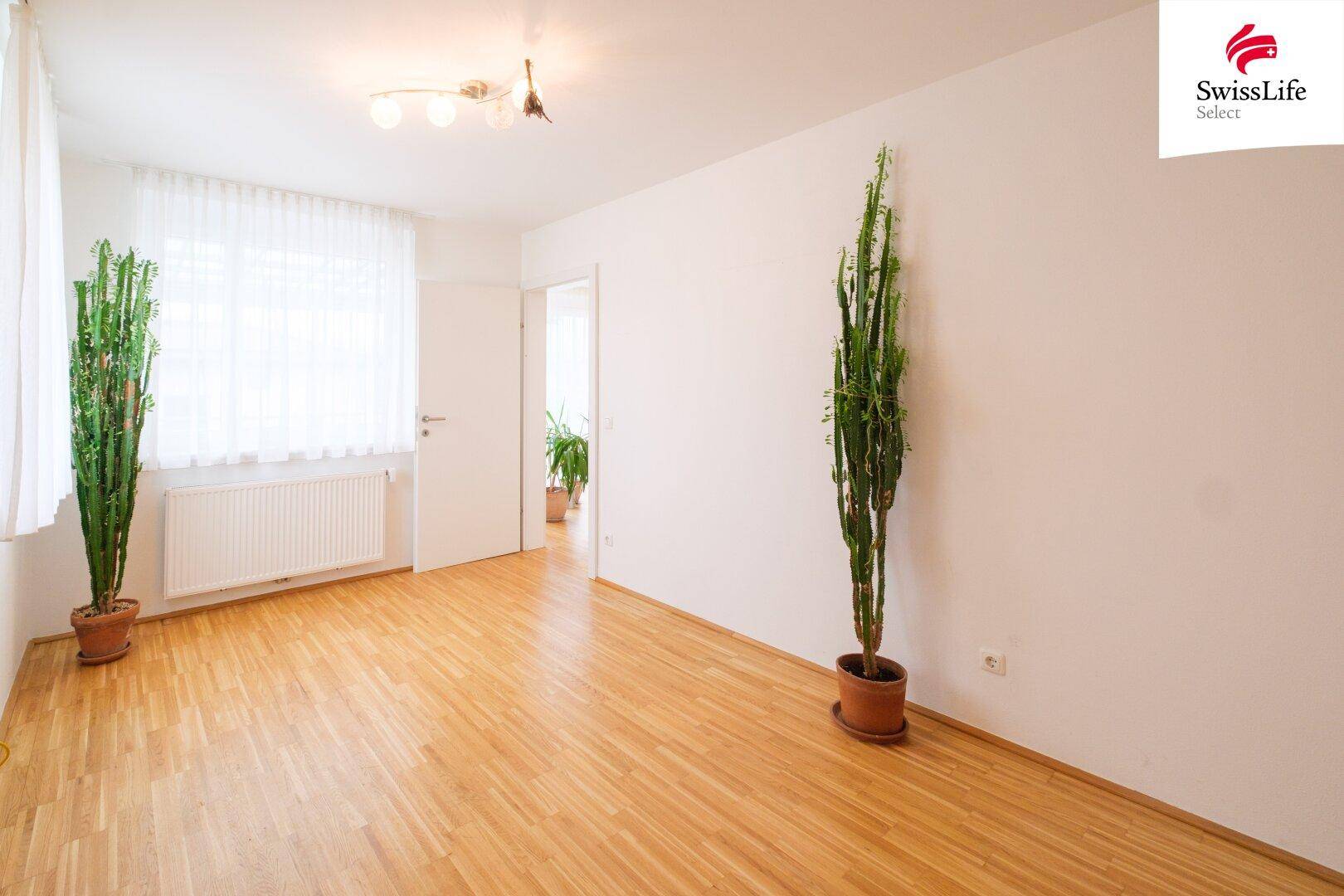 Geräumiges Wohnzimmer mit Parkettboden, hellen Wänden und viel Tageslicht durch große Fenster.