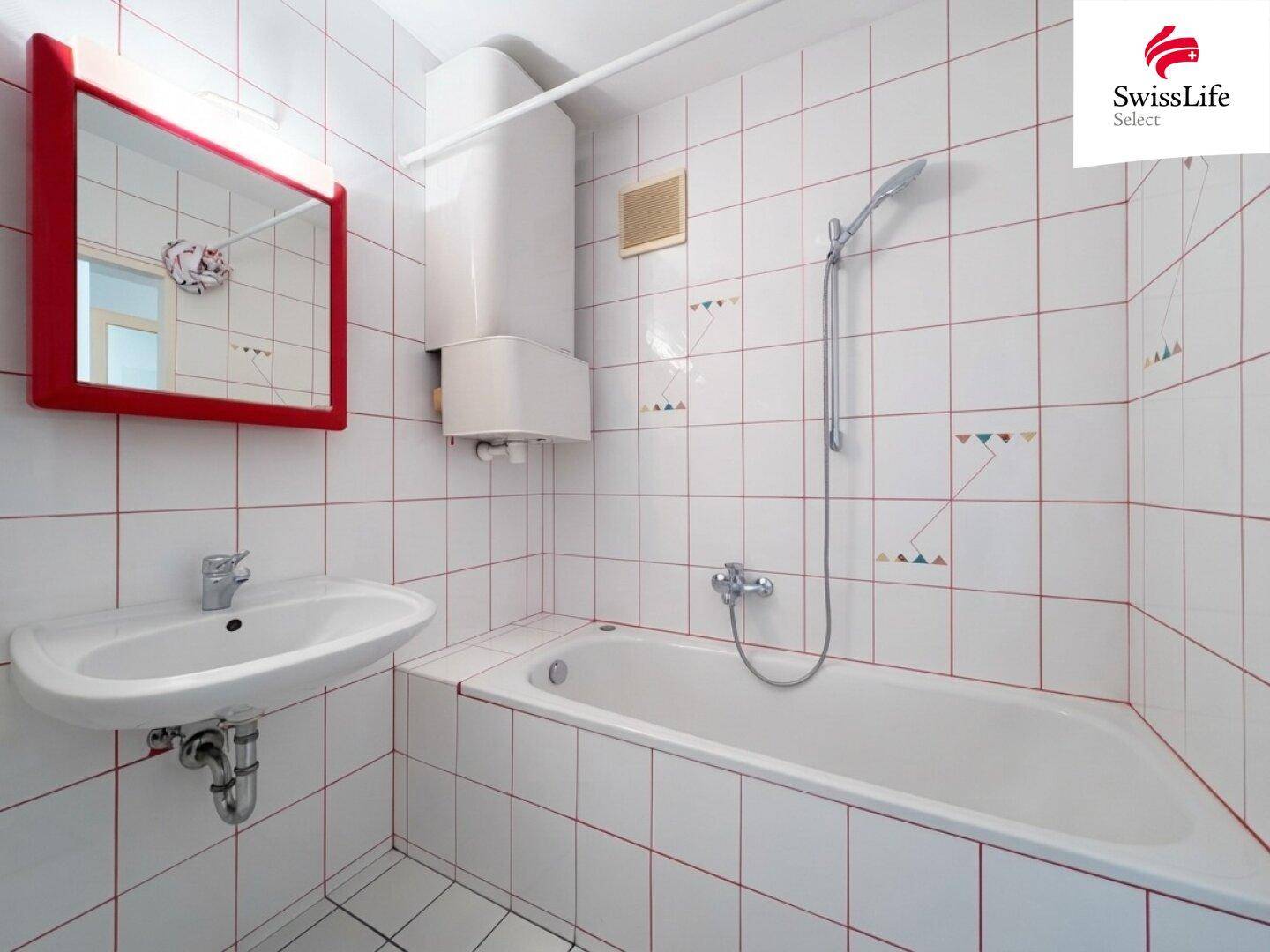 Funktionales Badezimmer mit Badewanne, Duschfunktion und weiß-roten Fliesen.