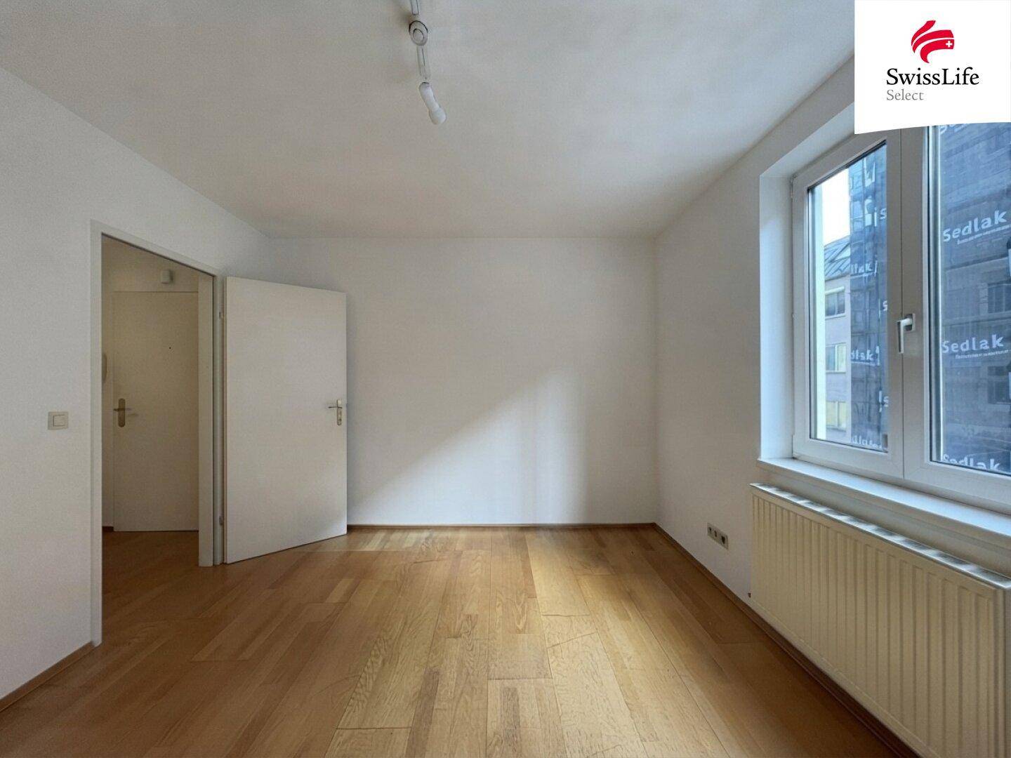 Geräumiges Zimmer mit Holzboden und Fenster, das sich ideal als Schlaf- oder Arbeitszimmer eignet.