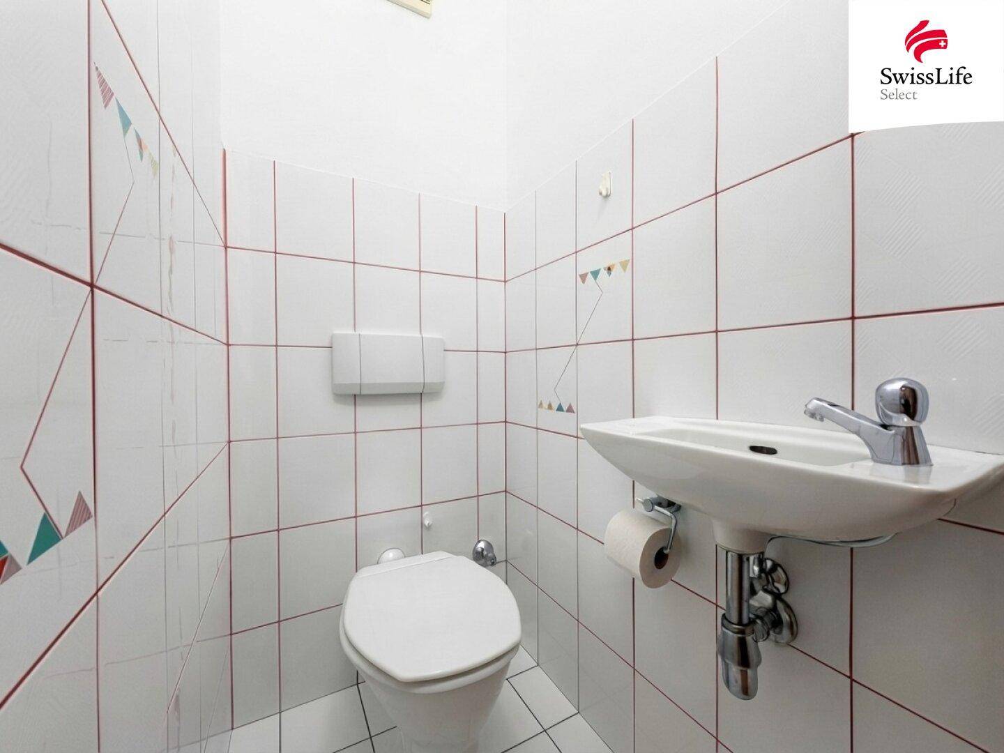 Separates WC mit Waschbecken und weißen Fliesen, ideal für Gäste.