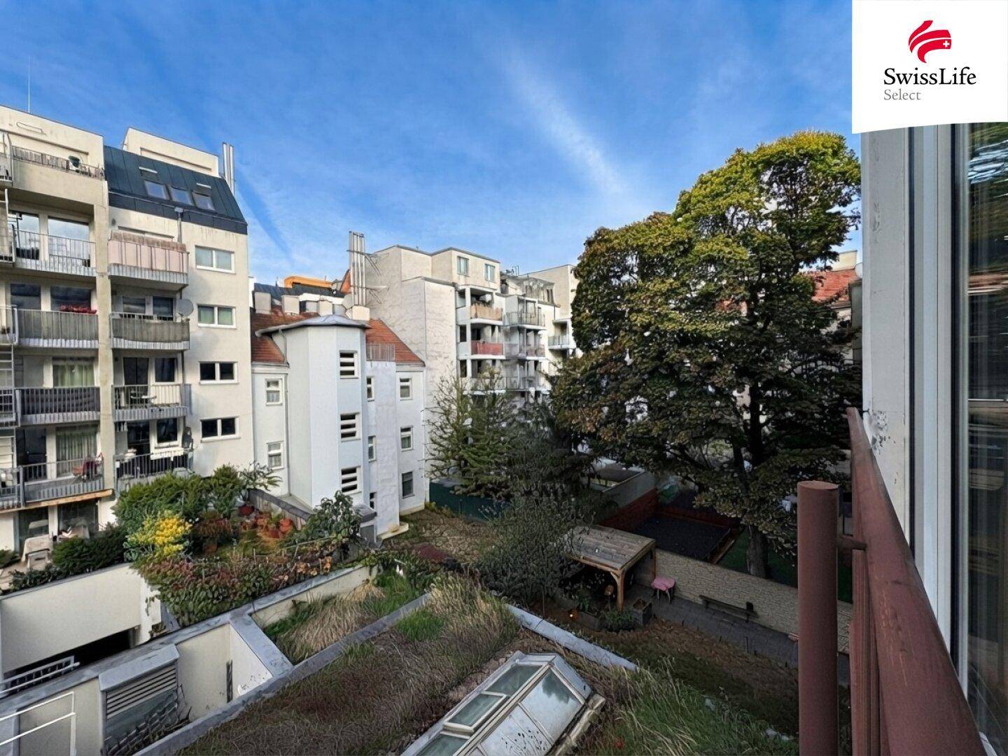 Blick auf einen begrünten Innenhof mit Bäumen und umliegenden Gebäuden.