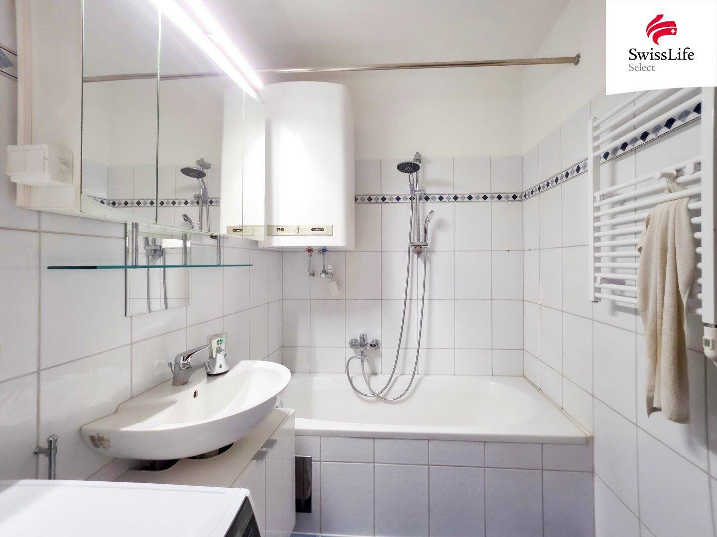 Badezimmer mit Badewanne, Waschbecken und weißer Fliesenverkleidung.
