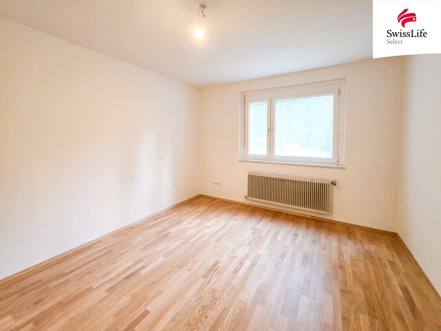 Geräumiges Schlafzimmer mit Parkettboden und einem großen Fenster für viel Tageslicht.