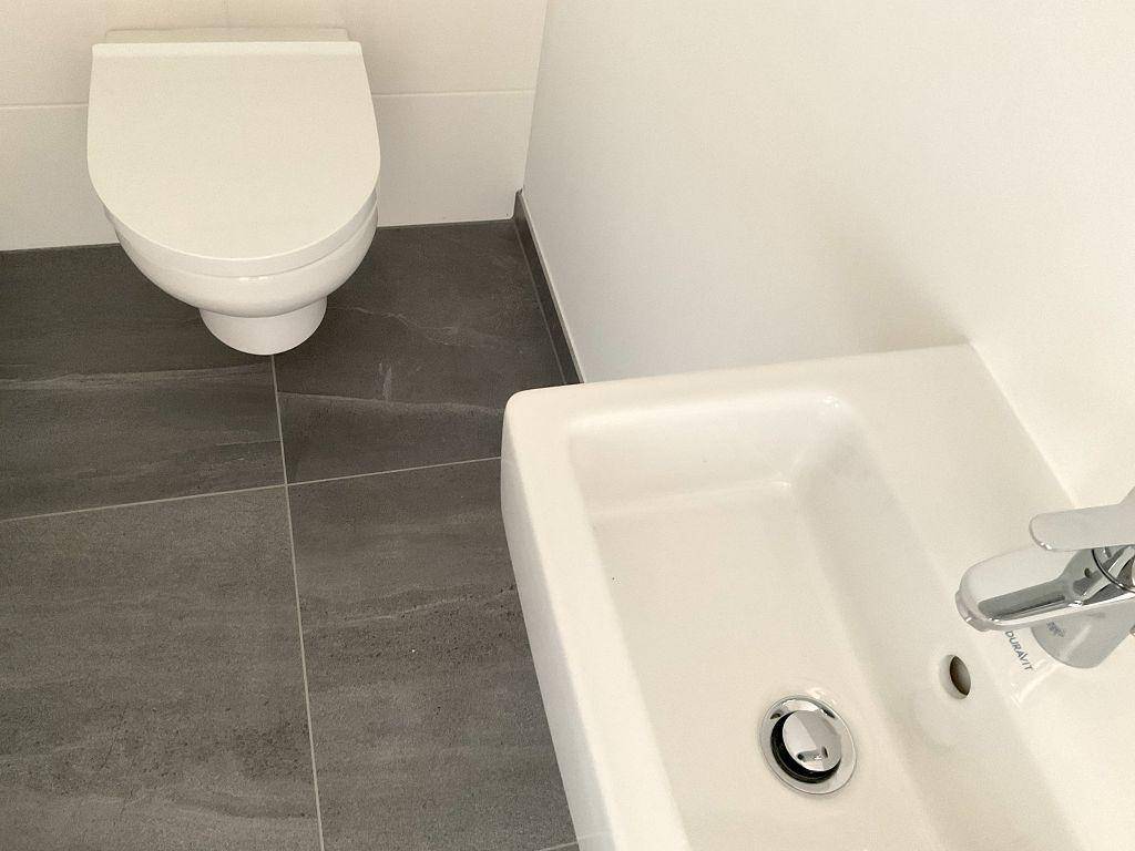 Modernes Gäste-WC mit wandmontierter Toilette und kleinem Waschbecken.