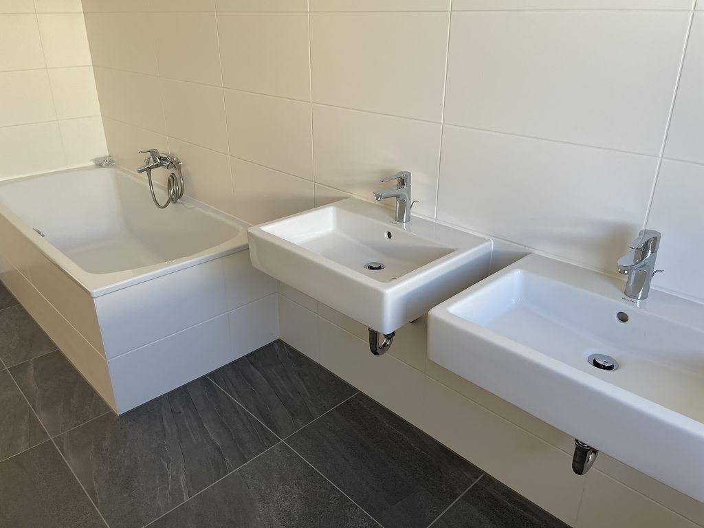 Modernes Badezimmer mit weißen Wandfliesen, dunklen Bodenfliesen, Badewanne und Doppelwaschbecken.