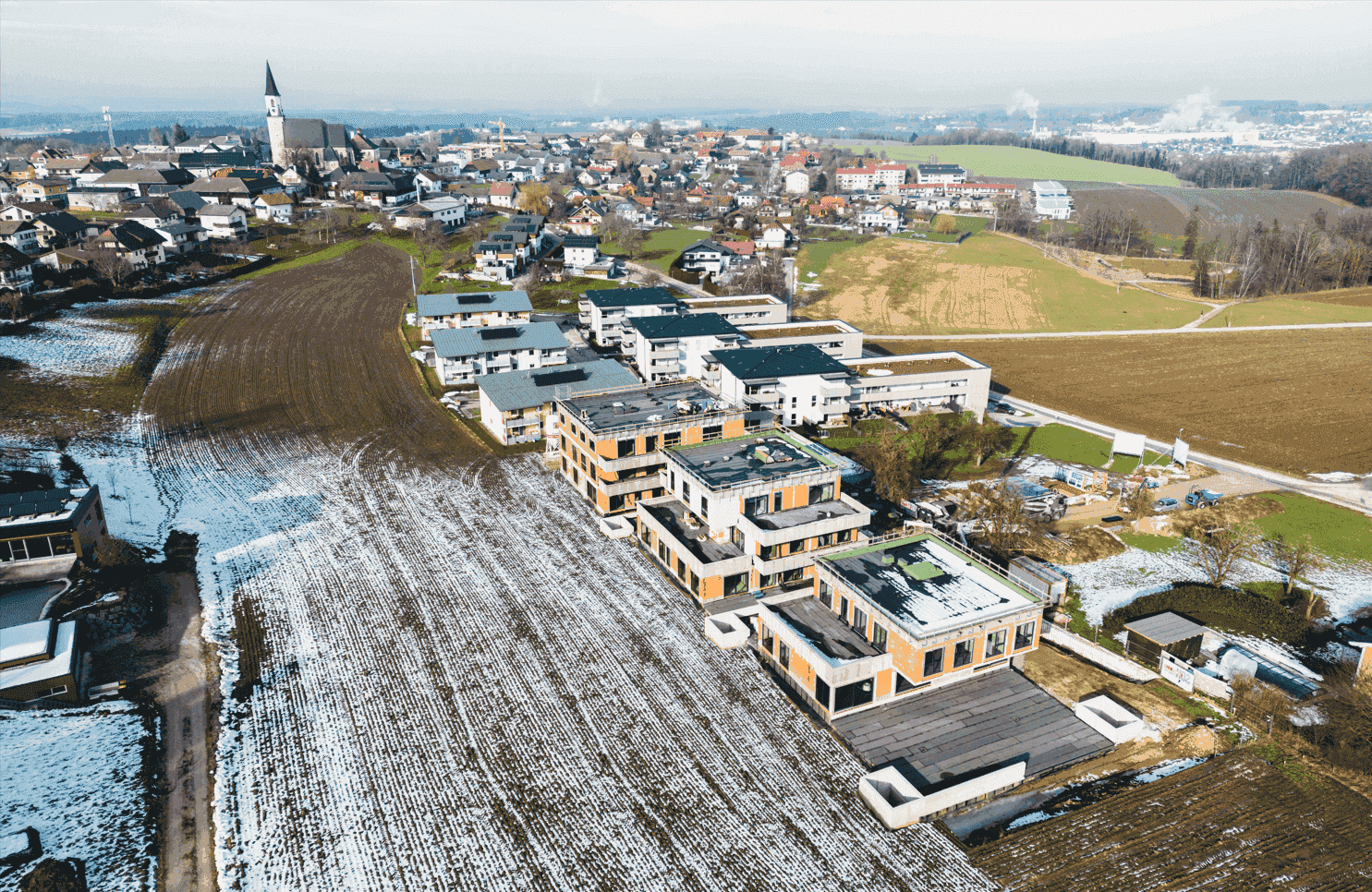 Luftaufnahme einer im Bau befindlichen Wohnanlage mit Blick auf eine nahegelegene Ortschaft.