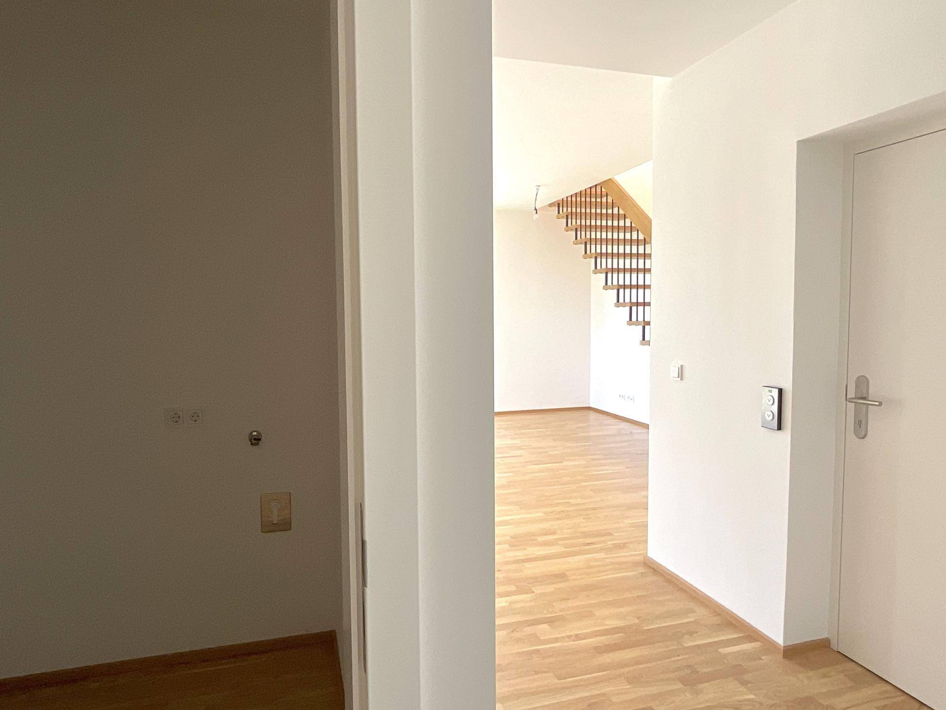 Heller Flur mit Parkettboden und Blick auf die offene Holztreppe.